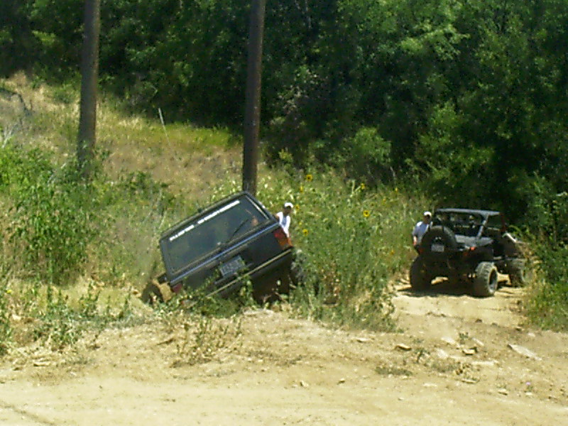 Dark Jeep Cherokee XJ tilted off-road with a side-by-side UTV nearby