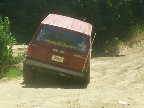 1986 Ford Bronco - A red Jeep Cherokee XJ is shown from the rear on a dirt path, leaning to the side.