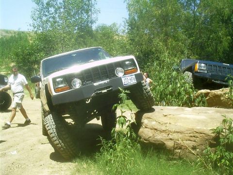 1986 Ford Bronco - Two Jeep Cherokee XJs navigate a rocky off-road course on a sunny day.