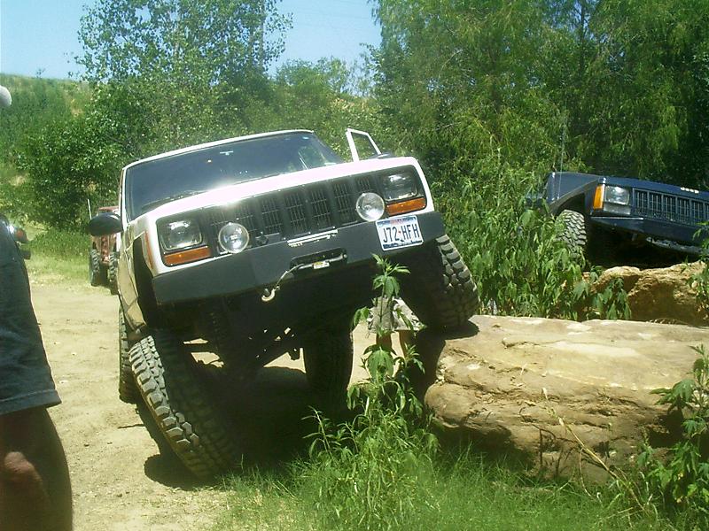 White Jeep Cherokee XJ with lifted suspension navigating rocks, license plate J72-HFH