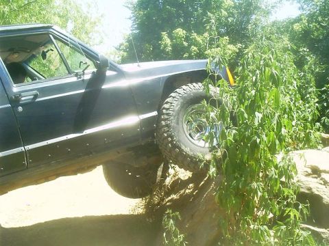 1986 Ford Bronco - Jeep Cherokee XJ navigating rough terrain with its tires on rocks and brush.