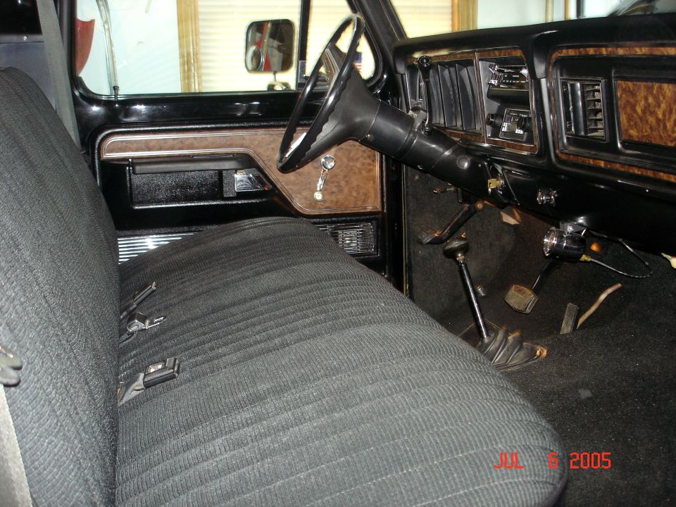 Black 1970s Ford pickup interior with cloth bench seat, woodgrain dash and floor shifters