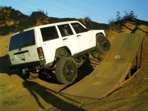 1986 Ford Bronco - This white Jeep Cherokee XJ is shown climbing a wooden ramp, demonstrating its off-road capabilities.