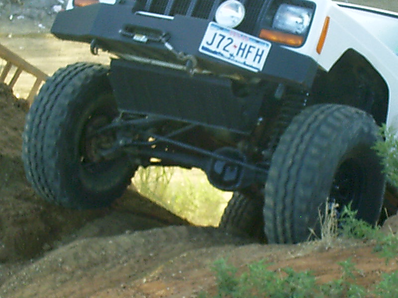 White Jeep Cherokee with aftermarket bumper and large tires on dirt terrain