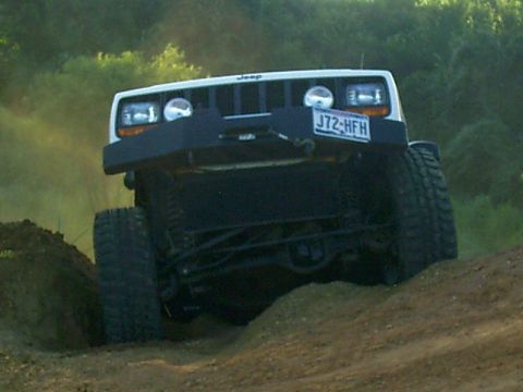 1986 Ford Bronco - A white Jeep Cherokee XJ navigates an off-road course, showing its front grille and tires.