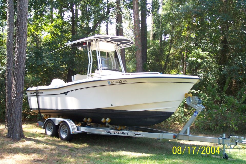 White Grady-White center console boat on a LoadRite tandem-axle trailer in a wooded yard, NJ 3925 GK.