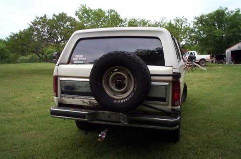 1985 Ford Bronco - Rear view of a 1985 Ford Bronco, showing its spare tire and a distant pickup truck.