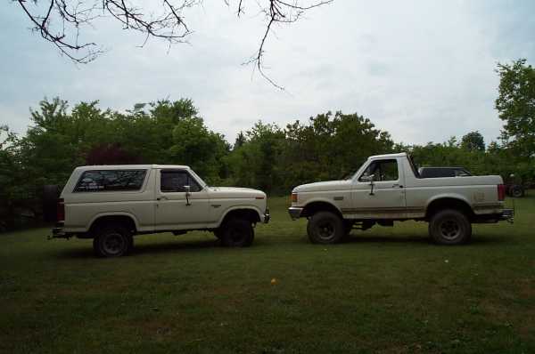 Two white Ford Broncos parked on grass, one is a Bronco SUV and the other is a Bronco pickup truck