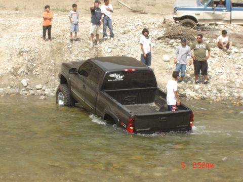 1977 Toyota Land Cruiser - A black pickup truck navigates through shallow water, observed by a group of onlookers on the bank.