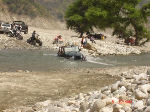 1977 Toyota Land Cruiser - Multiple off-road vehicles navigate a shallow, rocky riverbed under a bright sky.