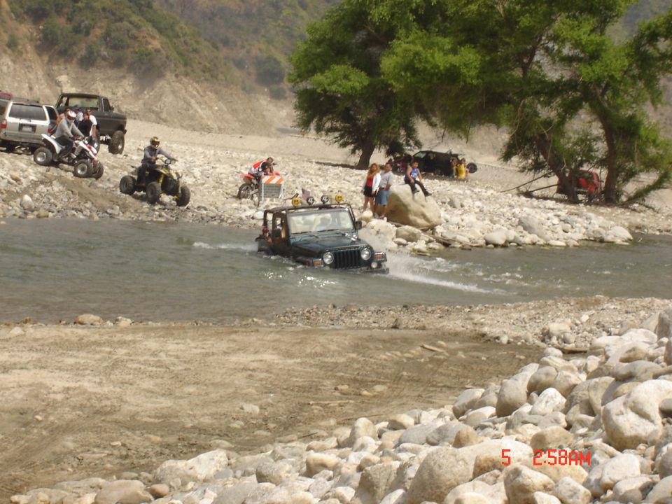 Black Jeep Wrangler driving through a rocky river, with two yellow lights on its roof