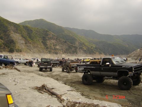 1977 Toyota Land Cruiser - A group of off-road vehicles are gathered in a dry riverbed with mountains in the background.