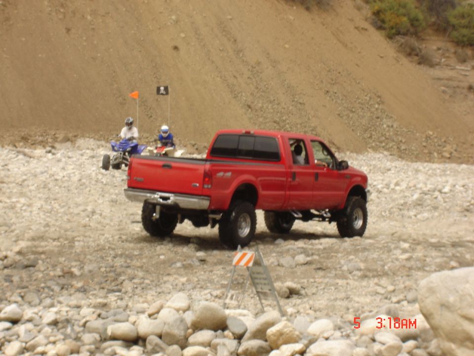 Lifted red Ford F-250 Super Duty crew cab parked on a rocky wash with quads behind