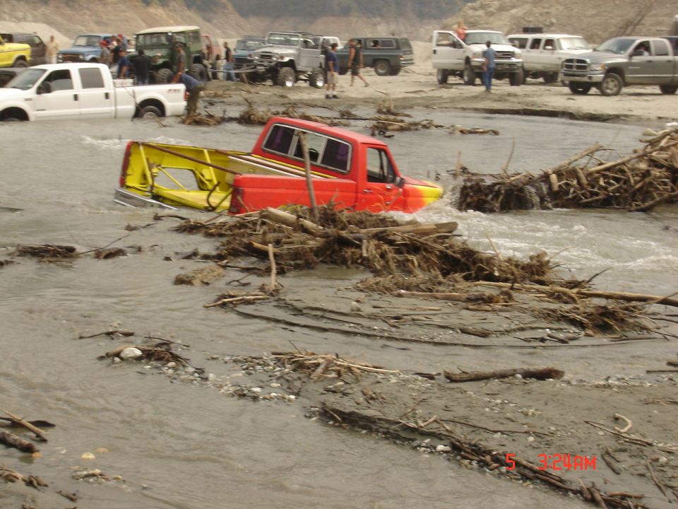 Red and yellow pickup truck stuck in river with debris