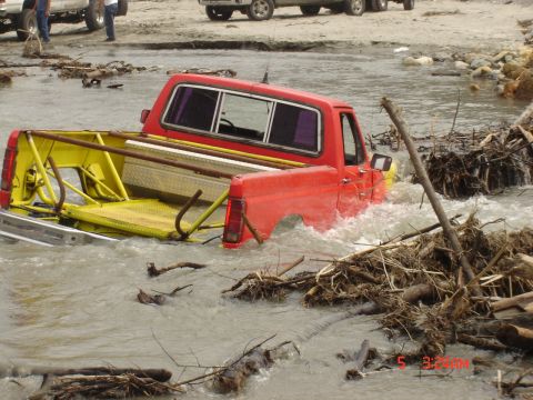 1977 Toyota Land Cruiser - A red pickup truck is partially submerged in fast-moving water, surrounded by debris.