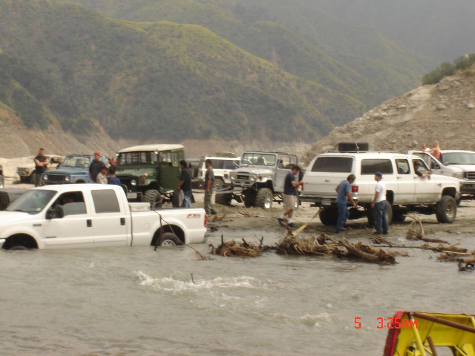 White Ford Super Duty FX4 crew cab stuck in muddy river water with FJ40s and a Suburban on the bank