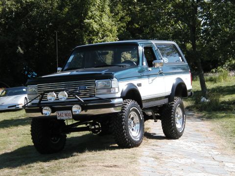 1994 Ford Bronco - Modified 1994 Ford Bronco with lifted suspension and large tires parked outdoors. Another car is visible in the background.