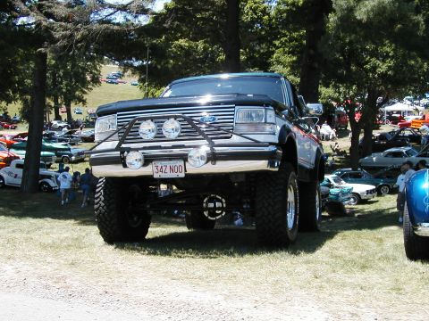 1994 Ford Bronco - A modified Ford Bronco is parked on grass at an outdoor car show with other vehicles in the background.