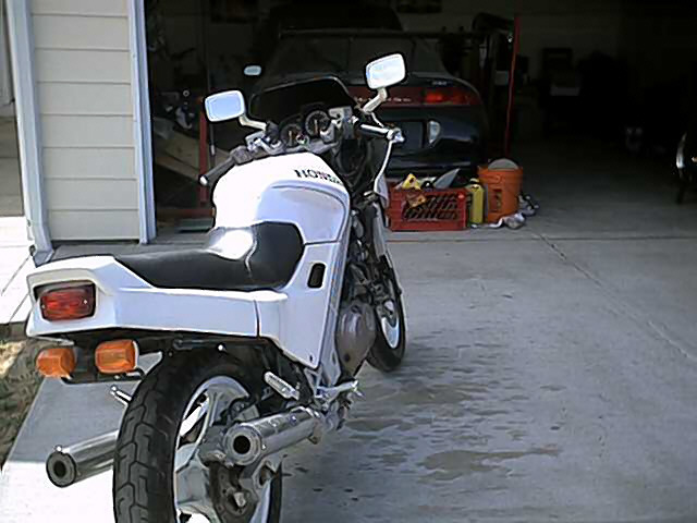 White Honda sport motorcycle parked rear-facing on driveway by open garage