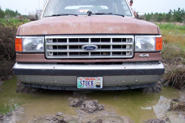 Front view of a brown Ford truck stuck in mud, with a Virginia license plate that says "STUCK"