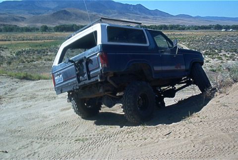 1986 Ford Bronco - A lifted Ford Bronco navigates a sandy incline in a dry, mountainous landscape.