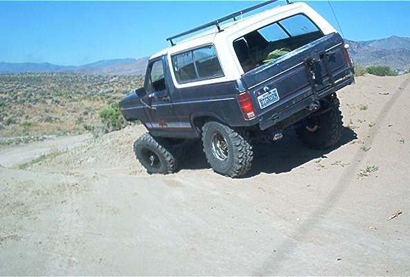 1986 Ford Bronco climbing a sandy incline with large off-road tires