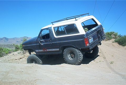 1986 Ford Bronco - This Ford Bronco is navigating a sandy incline under a clear blue sky.