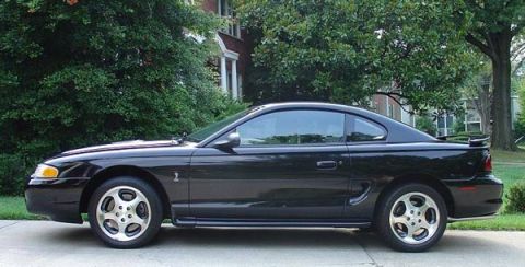 1988 Ford Bronco - A black Ford Mustang Cobra is parked in front of a house with trees in the background.