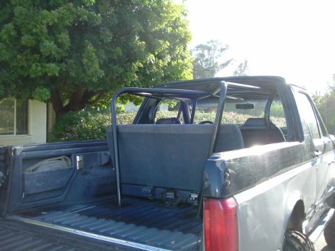 1989 Ford Bronco - The interior of a Ford Bronco shows rear seats and a roll cage, with the open truck bed in the foreground.