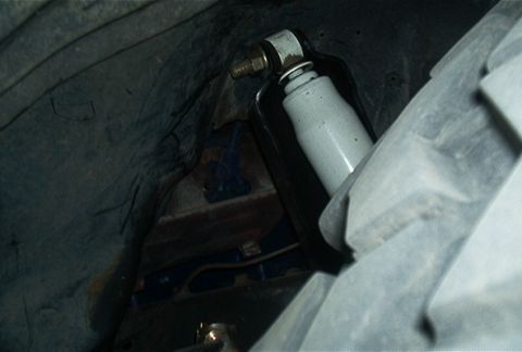 1986 Ford Bronco - A close-up view of a shock absorber assembly within the dark confines of a vehicle's wheel well.