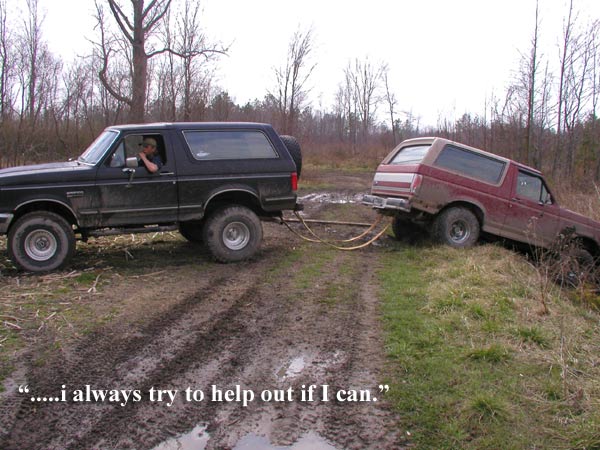 Side view of a black 1987 Ford Bronco towing a maroon Bronco out of a muddy ditch