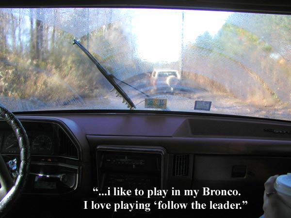 Interior view from driver's seat looking through a wet windshield at another vehicle ahead on a dirt road