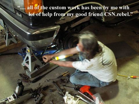 1988 Ford Bronco - A person is working on the front end of a vehicle that is supported by jack stands in a garage.