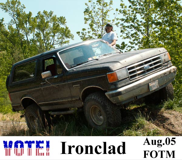 Dark Ford Bronco on grassy incline, front 3/4 view. Mud splatters on bumper and grille