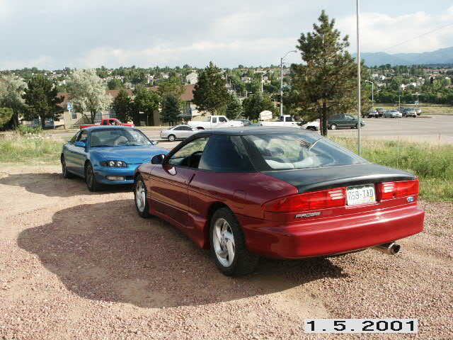 Dark red Ford Probe hatchback coupe with black roof and spoiler parked on gravel, rear 3/4 view