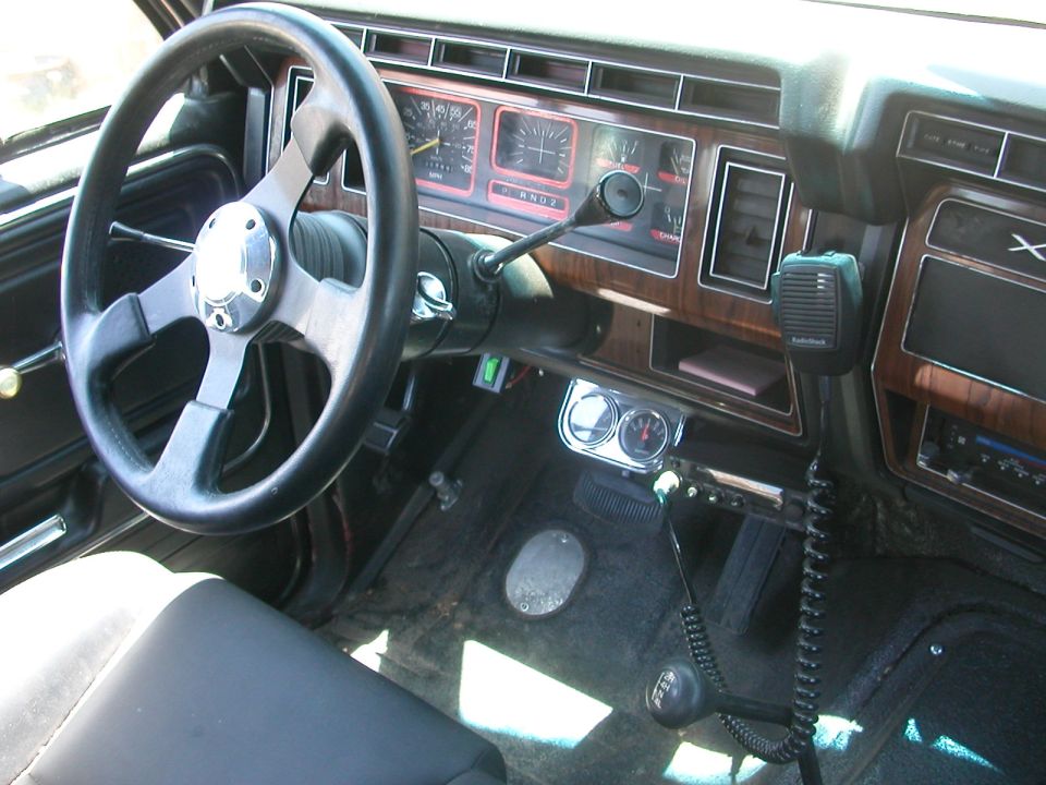 Interior view of a vehicle, showing an aftermarket steering wheel, dashboard gauges, and floor shifter