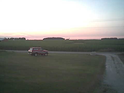 1994 Ford Bronco - A red 1994 Ford Bronco is seen driving on a dirt road during sunset with agricultural fields in the background.