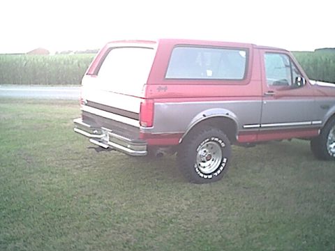 1994 Ford Bronco - This two-tone Ford Bronco is shown from the rear quarter angle, parked on a grassy field.