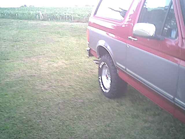 Red and gray Ford Bronco side view, showing the rear wheel and part of the door