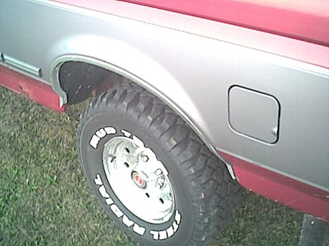 1994 Ford Bronco - Close-up of a two-tone silver and red Ford Bronco's rear fender and tire.