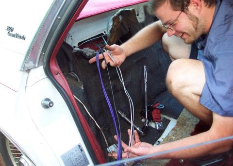 1985 Ford LTD Crown Victoria - A person works on wiring inside the trunk of a white car with red interior trim.