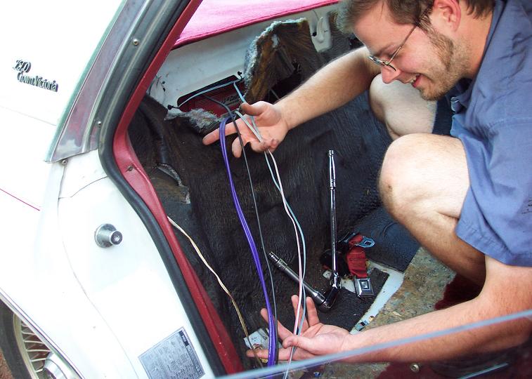 White car interior, red trim, dark carpet, person working on purple and white wires