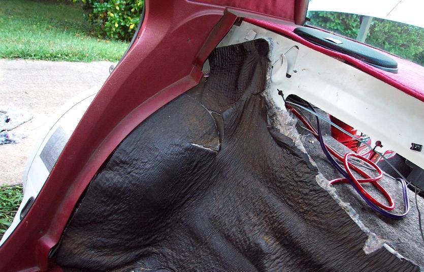 Red car trunk interior with exposed dark insulation and red and blue wires