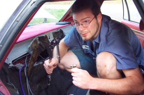 1985 Ford LTD Crown Victoria - Man works on the interior of a car, holding tools and appearing focused on the task.