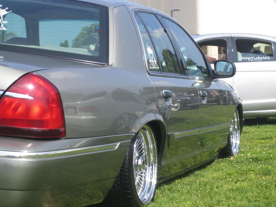 Lowered gray Mercury Grand Marquis on chrome wire wheels, rear quarter view on grass