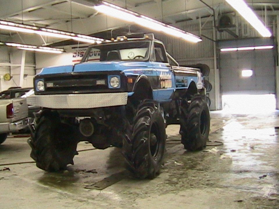 Blue vintage Chevy pickup mud truck on giant tractor tires inside a shop