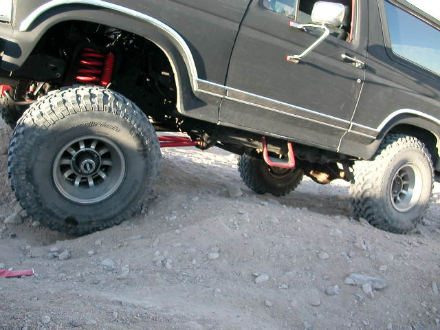 Black 1984 Ford Bronco with large tires and red suspension components on rocky terrain