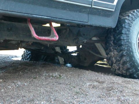 1984 Ford Bronco - Undercarriage view shows a red tow hook and large off-road tires on a vehicle.