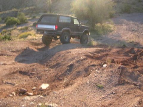 1984 Ford Bronco - A black Ford Bronco navigates a challenging dirt terrain with steep inclines and loose soil.