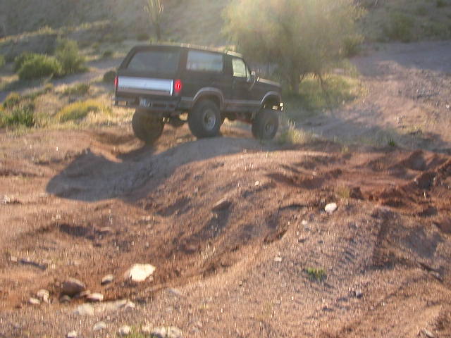 Black Ford Bronco climbing a dirt hill off-road. Lifted suspension and large tires visible